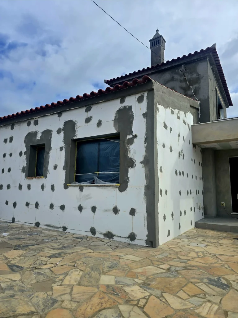 Fachada em reabilitação com sistema ETICS (Capoto) em placas de isolamento branco, fixadas com argamassa e pontos de adesivo cinzento à volta de janelas protegidas.